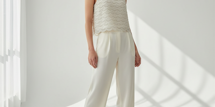 Woman wearing a sleeveless lace top and white pants in a bright room with sunlight filtering through.