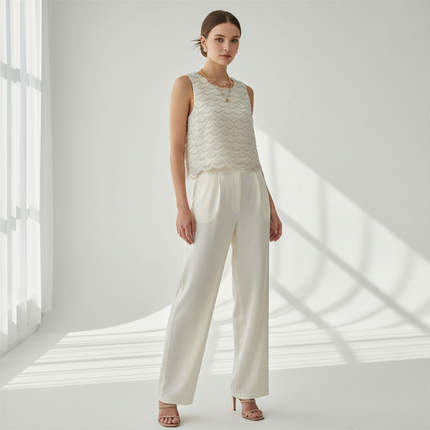 Woman wearing a sleeveless lace top and white pants in a bright room with sunlight filtering through.