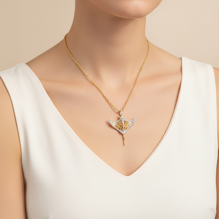 A close-up of a model wearing a delicate gold chain necklace with a stylized bird pendant featuring white and gold details, paired with a white sleeveless top against a warm beige background.