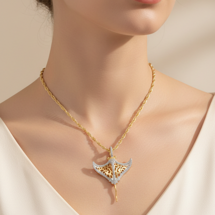 A close-up of a model wearing a gold chain necklace with a winged pendant featuring gold and silver detailing, styled with a white V-neck top against a warm beige background.